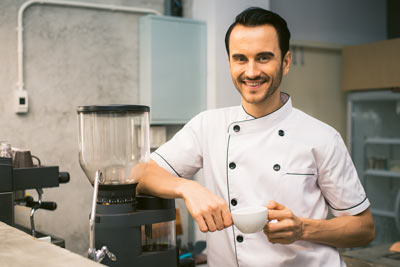 man leaning on coffee grinder with a cup in his hand